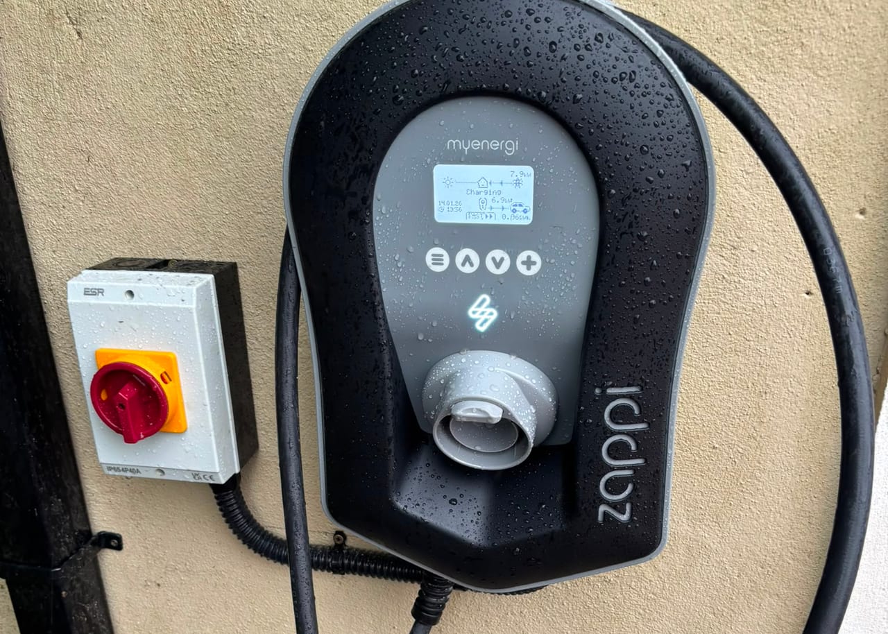 A wall-mounted home EV charger and its isolator, the screen showing the car charging at 6.9 kW from solar generation