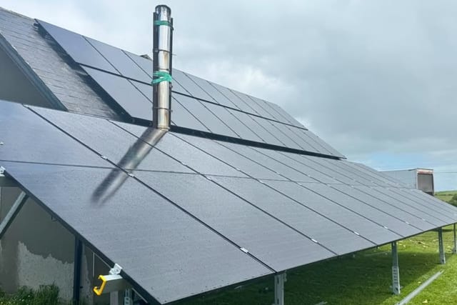 A ground-mounted solar array on a frame beside a house, angled towards the sky