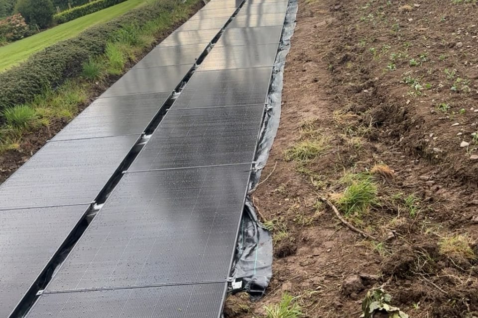 A ground-mounted solar array running along the edge of a field