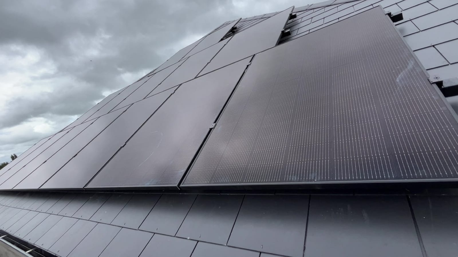 An all-black solar array fitted flush across a slate roof, seen from low along the panel run
