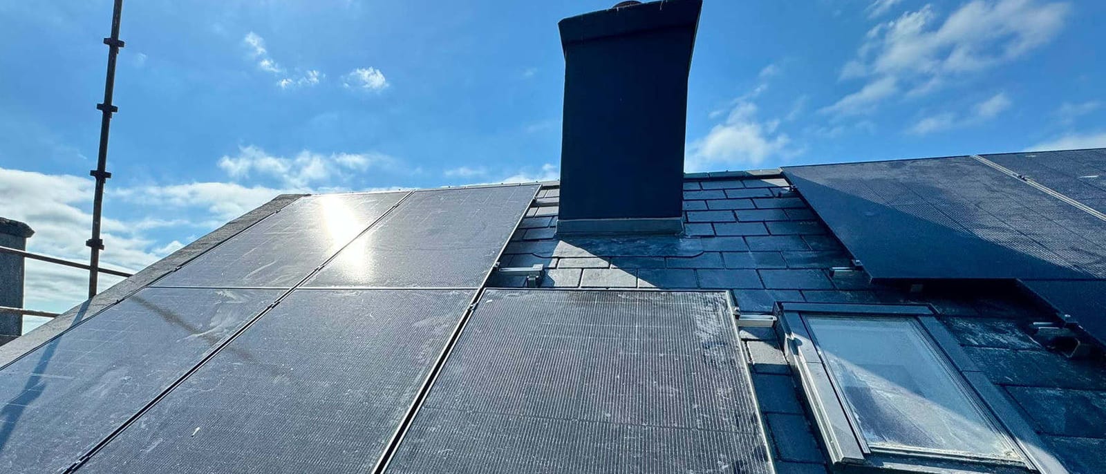 The same slate roof with the solar array complete, panels sitting flush either side of the chimney